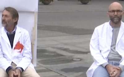 A pair of hunger-striking doctors, their white coats stained with mock blood, sit outside the Swiss parliament building in Bern, Switzerland, in a video published on September 8, 2025. (Used in accordance with Clause 27a of the Copyright Law)